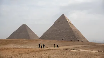 Tourists seen taking photos of the Great Pyramids of Giza from the desert in Egypt - an iconic archaeological and travel destination.
