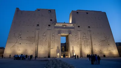 Temple of Edfu illuminated at dawn - golden lights highlight the ancient structure as the sky transitions from night to day in Edfu, Egypt.