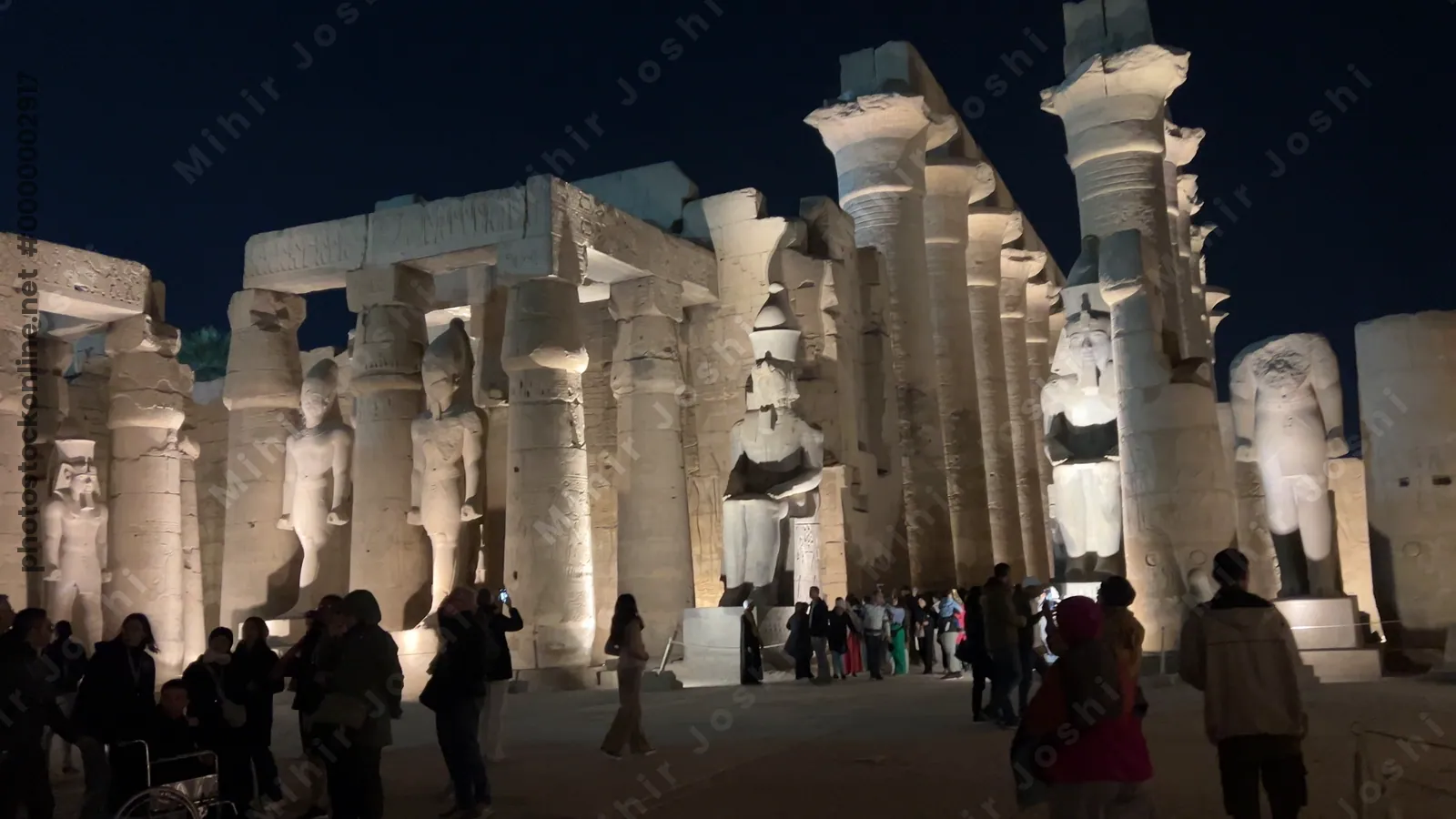 Luxor, Egypt - Feb 9, 2025: Footage of the illuminated colonnade and colossal statues of Luxor Temple at night in Egypt, with tourists exploring the ancient site.