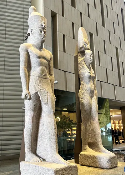 Massive statues of a Ptolemaic queen and king discovered in sunken Thonis-Heracleion, displayed at the Grand Egyptian Museum near Cairo.