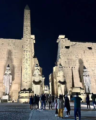 Luxor, Egypt - Feb 9, 2025: Illuminated entrance of Luxor Temple at night with colossal statues and a standing obelisk, with visitors in the foreground.