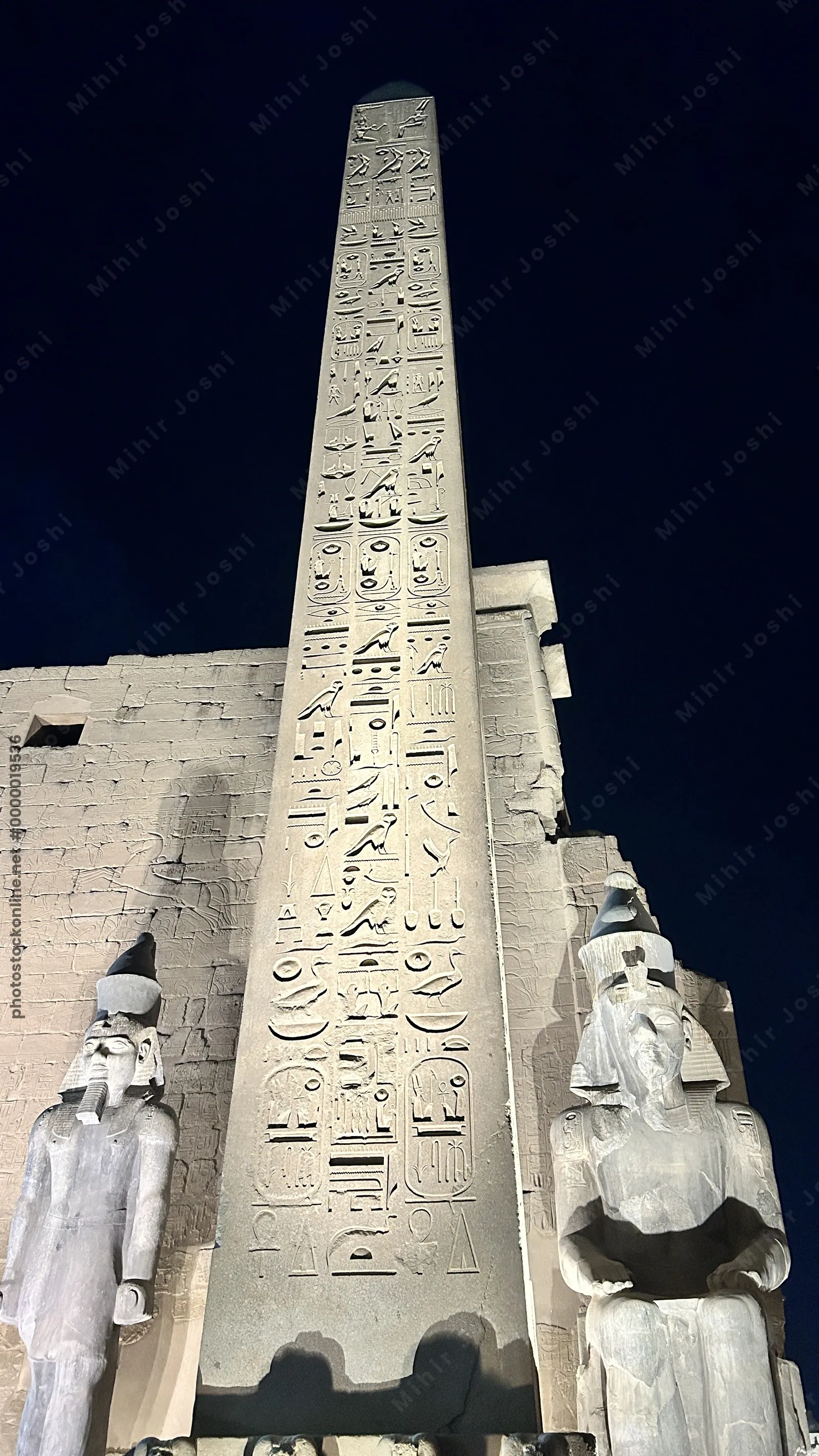 Luxor, Egypt - Feb 9, 2025: Night view of the illuminated obelisk and colossal statues at the entrance pylon of Luxor Temple in Egypt, with hieroglyphs carved in stone.