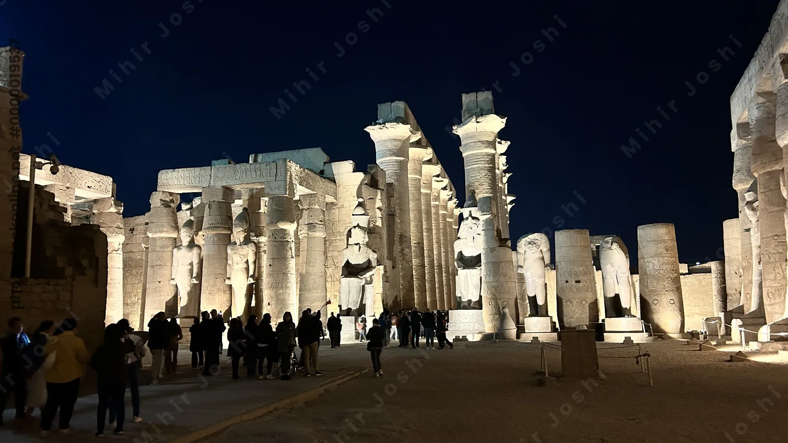 Luxor, Egypt - Feb 9, 2025: Night view of Luxor Temple with illuminated statues and towering hypostyle hall columns, with visitors walking through the ancient complex in Egypt.