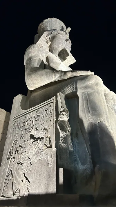 Luxor, Egypt - Feb 9, 2025: Illuminated colossal statue of Ramses II at Luxor Temple with hieroglyphic reliefs carved on the throne, viewed at night from a low angle in Egypt.