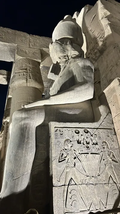 Luxor, Egypt - Feb 9, 2025: Illuminated colossal statue of Ramses II at Luxor Temple with hieroglyphic reliefs carved on the throne, viewed at night from a low angle in Egypt.