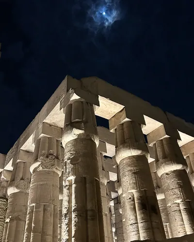 Luxor, Egypt - Feb 9, 2025: Night view of illuminated pillars of Luxor Temple with the moon in the sky partly shrouded by clouds in Luxor, Egypt.