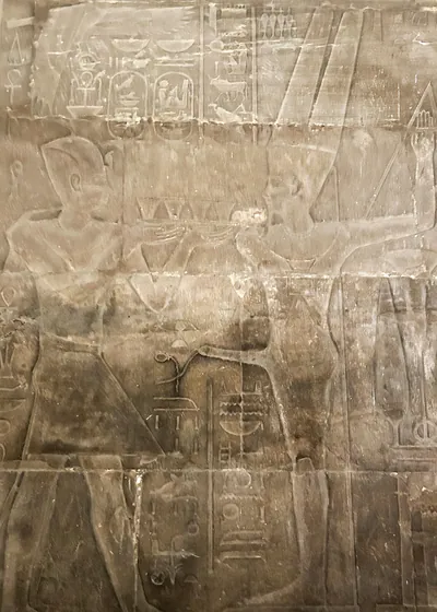 Edfu, Egypt - Feb 9, 2025: Ancient wall relief showing a pharaoh making an offering before Min, the fertility god of ancient Egypt, represented with erect phallus.