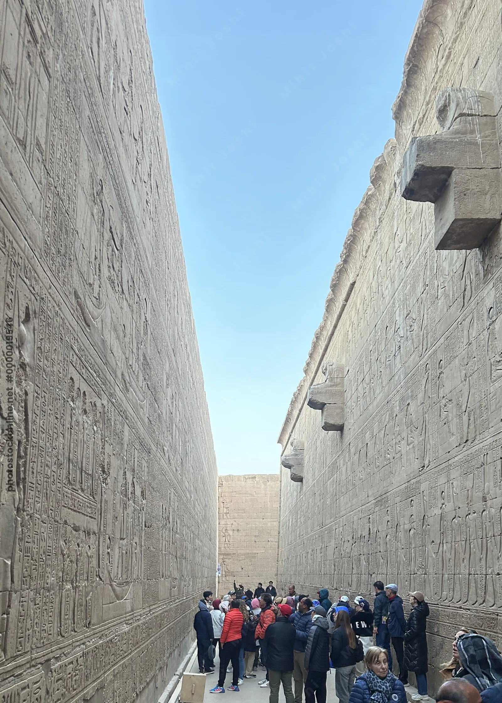 Edfu, Egypt - Feb 9, 2025: Tourists walking through a narrow passage inside the Temple of Edfu in Egypt, with ancient wall reliefs and hieroglyphic inscriptions on both sides.