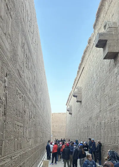 Edfu, Egypt - Feb 9, 2025: Tourists walking through a narrow passage inside the Temple of Edfu in Egypt, with ancient wall reliefs and hieroglyphic inscriptions on both sides.