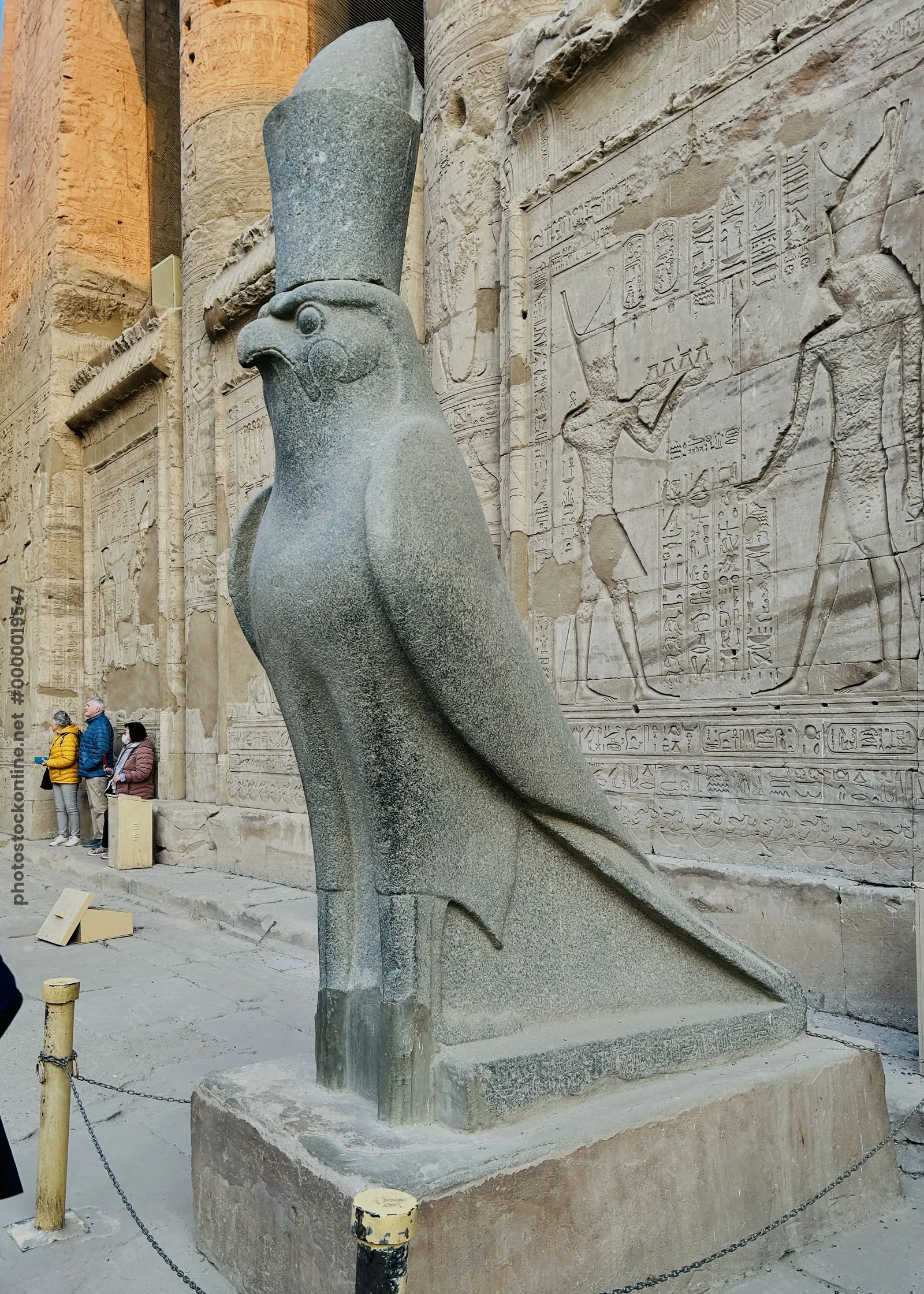 Edfu, Egypt - Feb 9, 2025: Granite statue of the falcon-headed god Horus at the Temple of Edfu in Egypt, wearing the double crown and standing before carved reliefs.