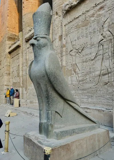 Edfu, Egypt - Feb 9, 2025: Granite statue of the falcon-headed god Horus at the Temple of Edfu in Egypt, wearing the double crown and standing before carved reliefs.