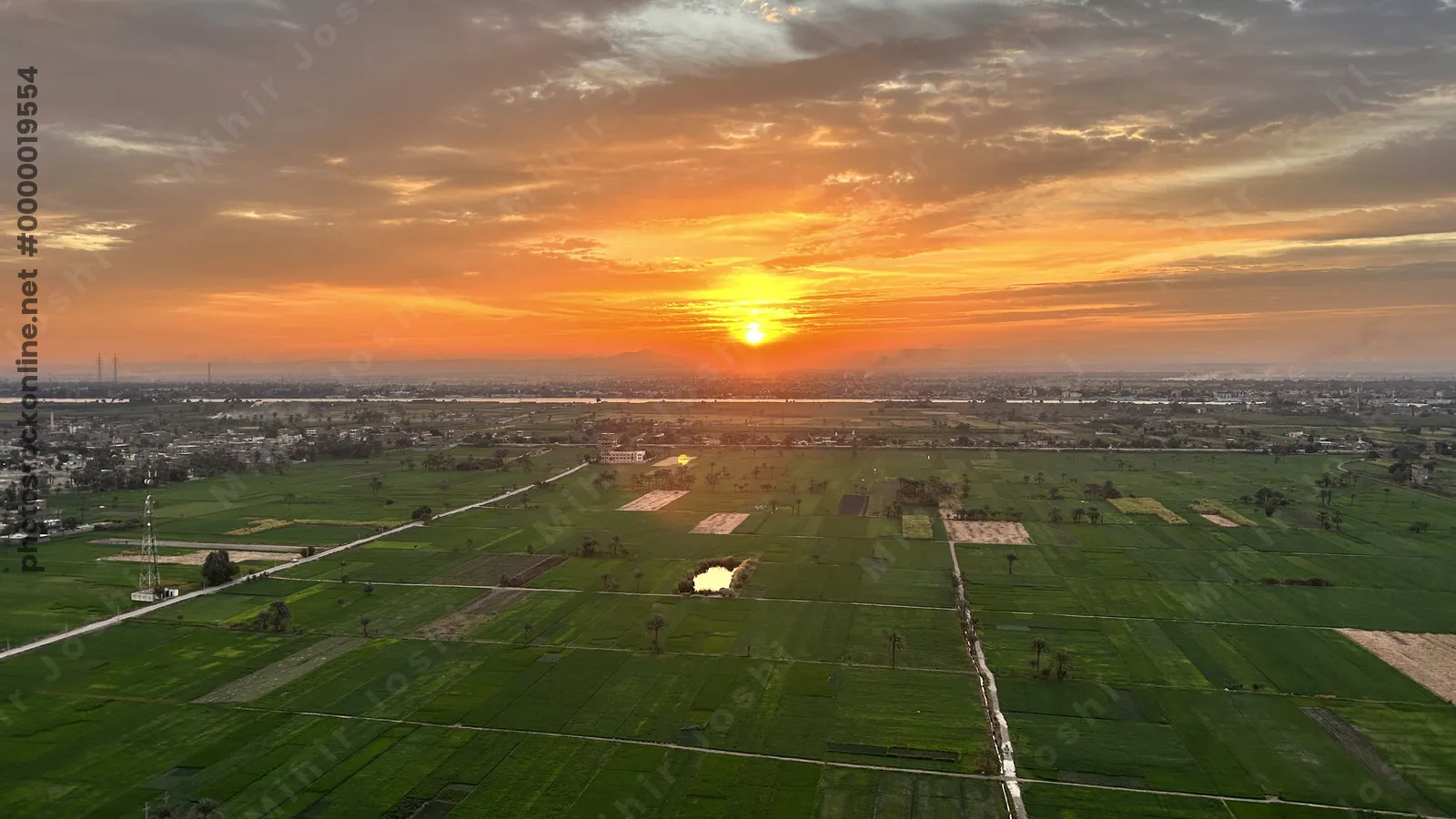 Sunrise over green agricultural fields near the Nile River in Luxor, Egypt, with farmland and glowing sky on the horizon.