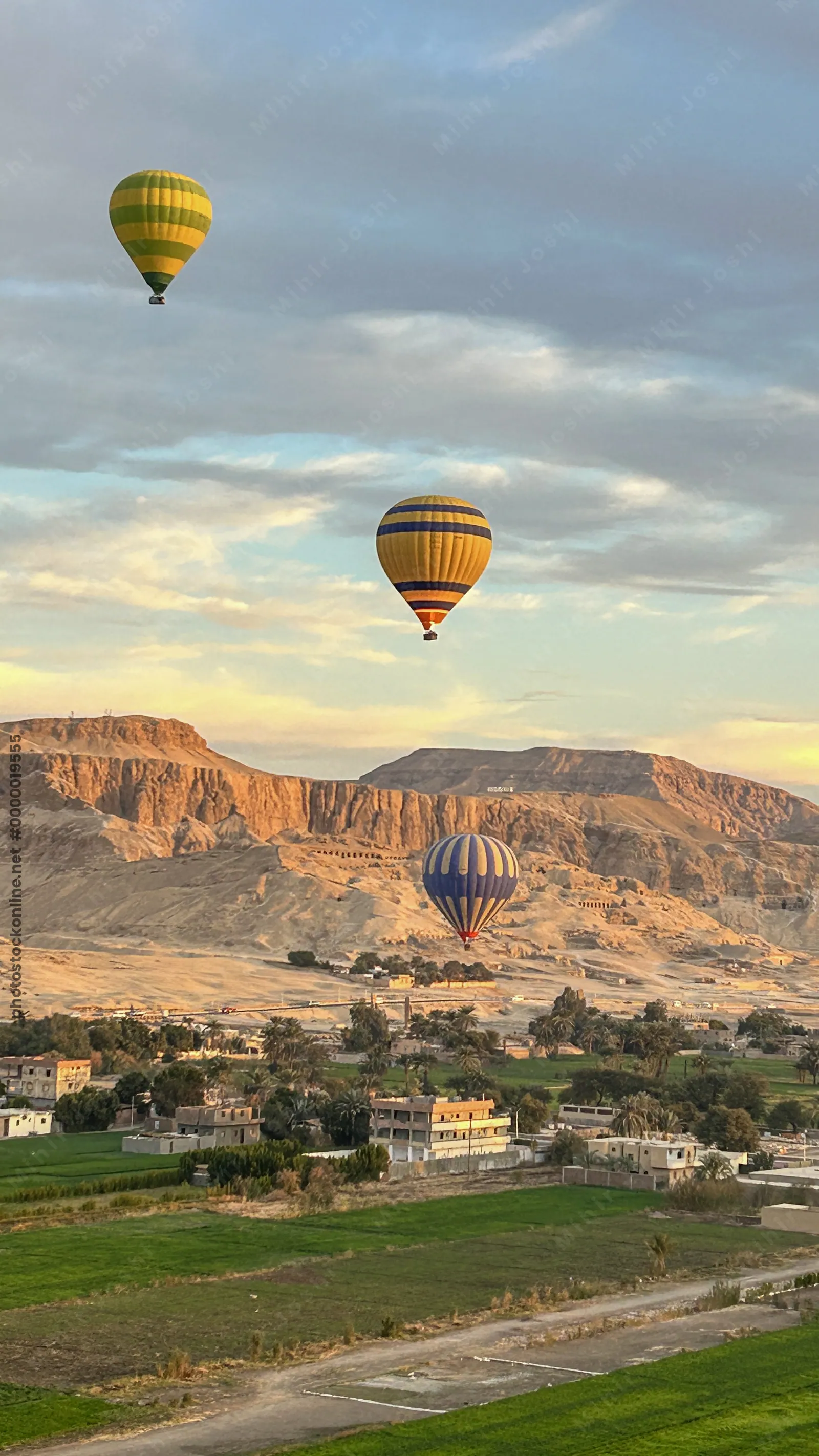 Luxor, Egypt - Feb 10, 2025: Hot air balloons at sunrise floating above green fields and cliffs of Luxor, Egypt, with the Theban mountains in the background.