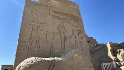 Dendera, Egypt - Feb 10, 2025: View of the entrance gate of the Hathor Temple enclosure with detailed wall reliefs and an acephalous sphinx statue of the dromos.