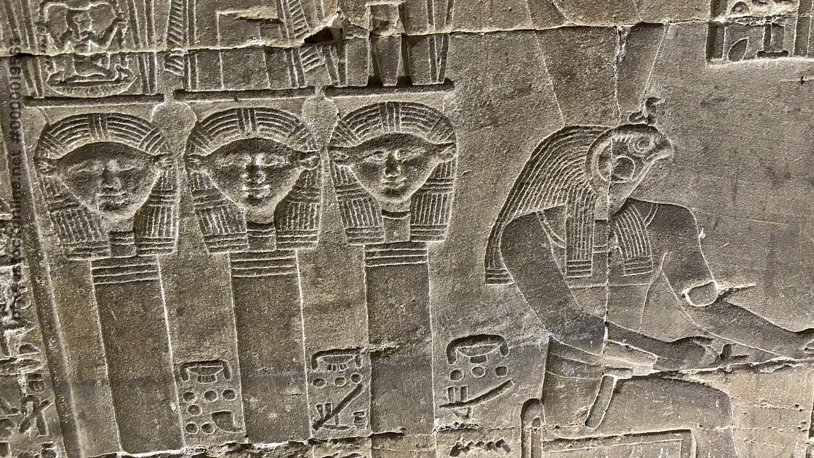Dendera, Egypt - Feb 10, 2025: Ancient wall relief at the Temple of Hathor depicting Hathor heads alongside a falcon-headed figure with hieroglyphic inscriptions.