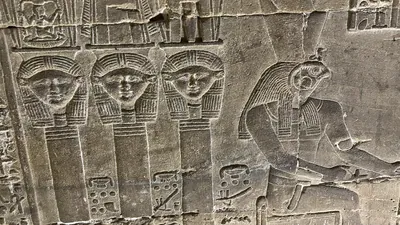 Dendera, Egypt - Feb 10, 2025: Ancient wall relief at the Temple of Hathor depicting Hathor heads alongside a falcon-headed figure with hieroglyphic inscriptions.
