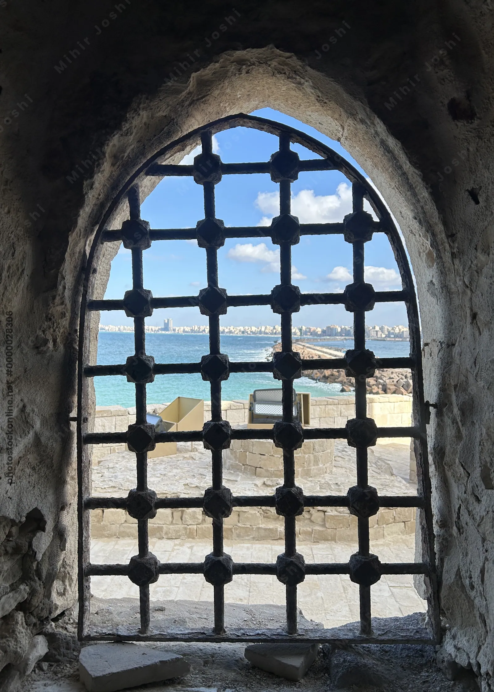 Alexandria, Egypt - Feb 13, 2025: Arched stone window with iron bars at the Citadel of Qaitbay fortress overlooking the Mediterranean coast.