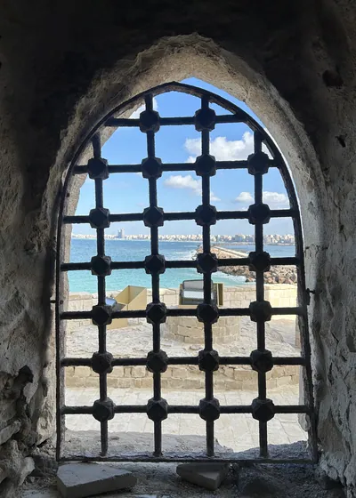Alexandria, Egypt - Feb 13, 2025: Arched stone window with iron bars at the Citadel of Qaitbay fortress overlooking the Mediterranean coast.