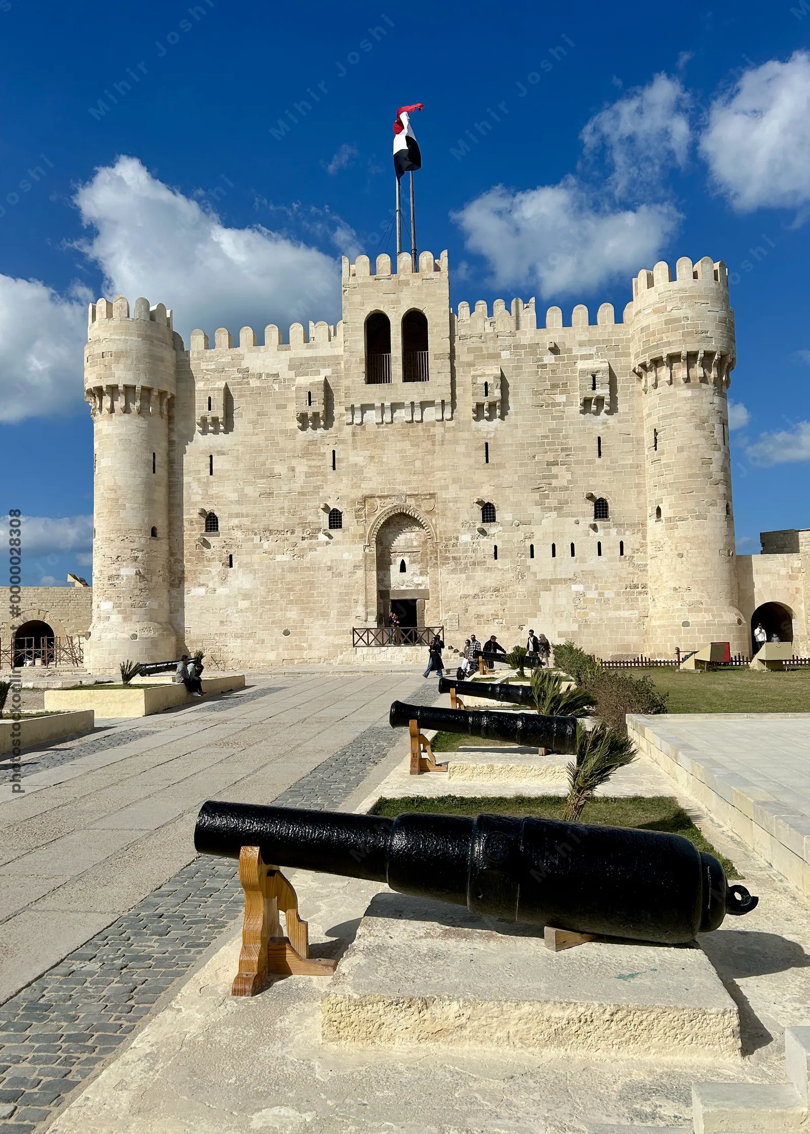 Alexandria, Egypt - Feb 13, 2025: Visitors at the medieval Citadel of Qaitbay fortress with Egyptian flag and cannons on display.