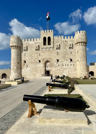 Alexandria, Egypt - Feb 13, 2025: Visitors at the medieval Citadel of Qaitbay fortress with Egyptian flag and cannons on display.