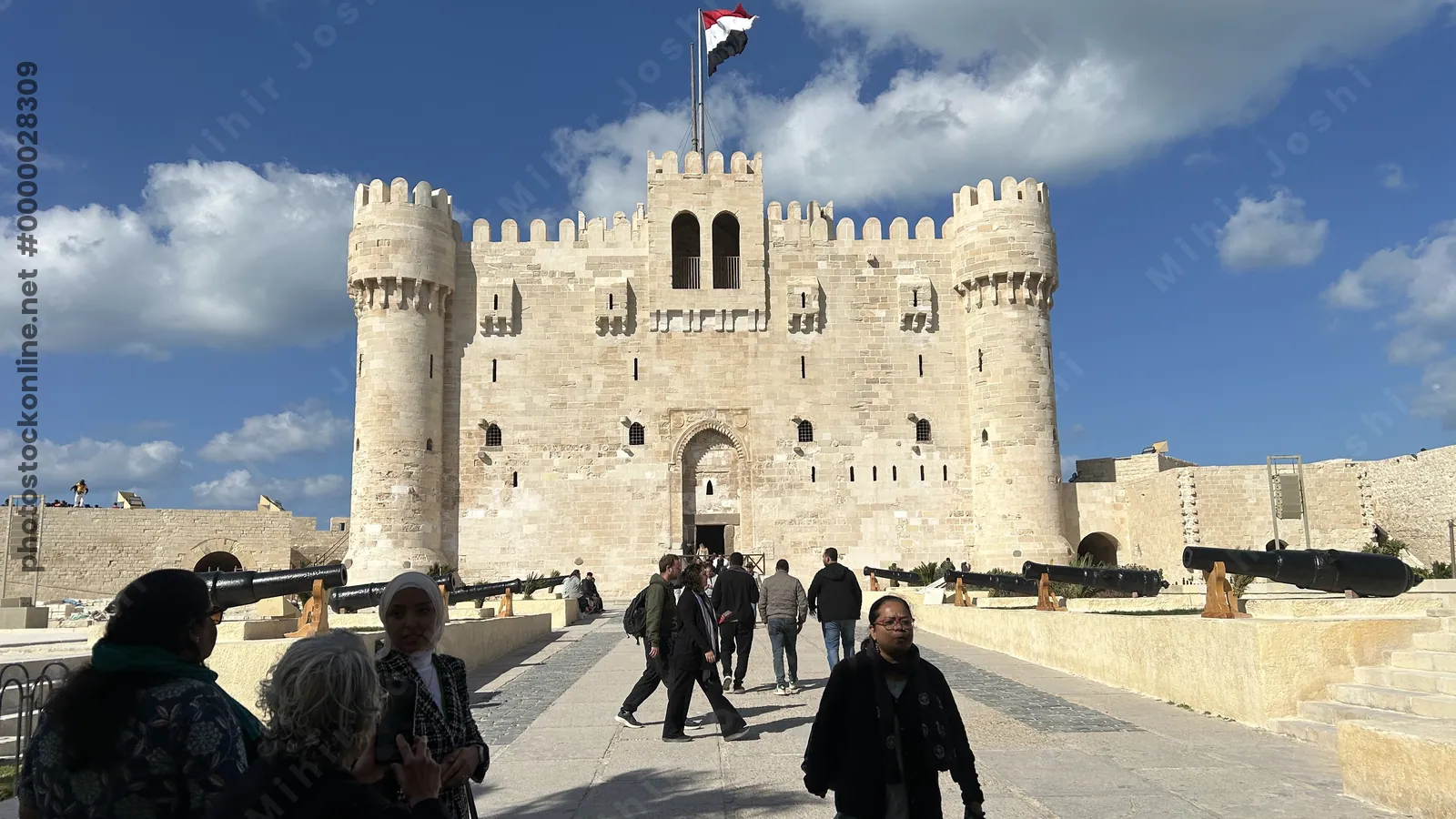 Alexandria, Egypt - Feb 13, 2025: Visitors at the medieval Citadel of Qaitbay fortress with Egyptian flag and cannons on display.