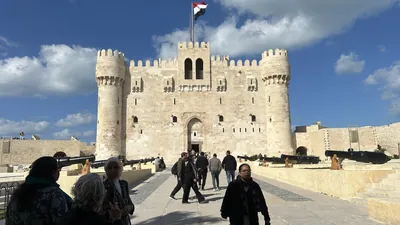 Alexandria, Egypt - Feb 13, 2025: Visitors at the medieval Citadel of Qaitbay fortress with Egyptian flag and cannons on display.