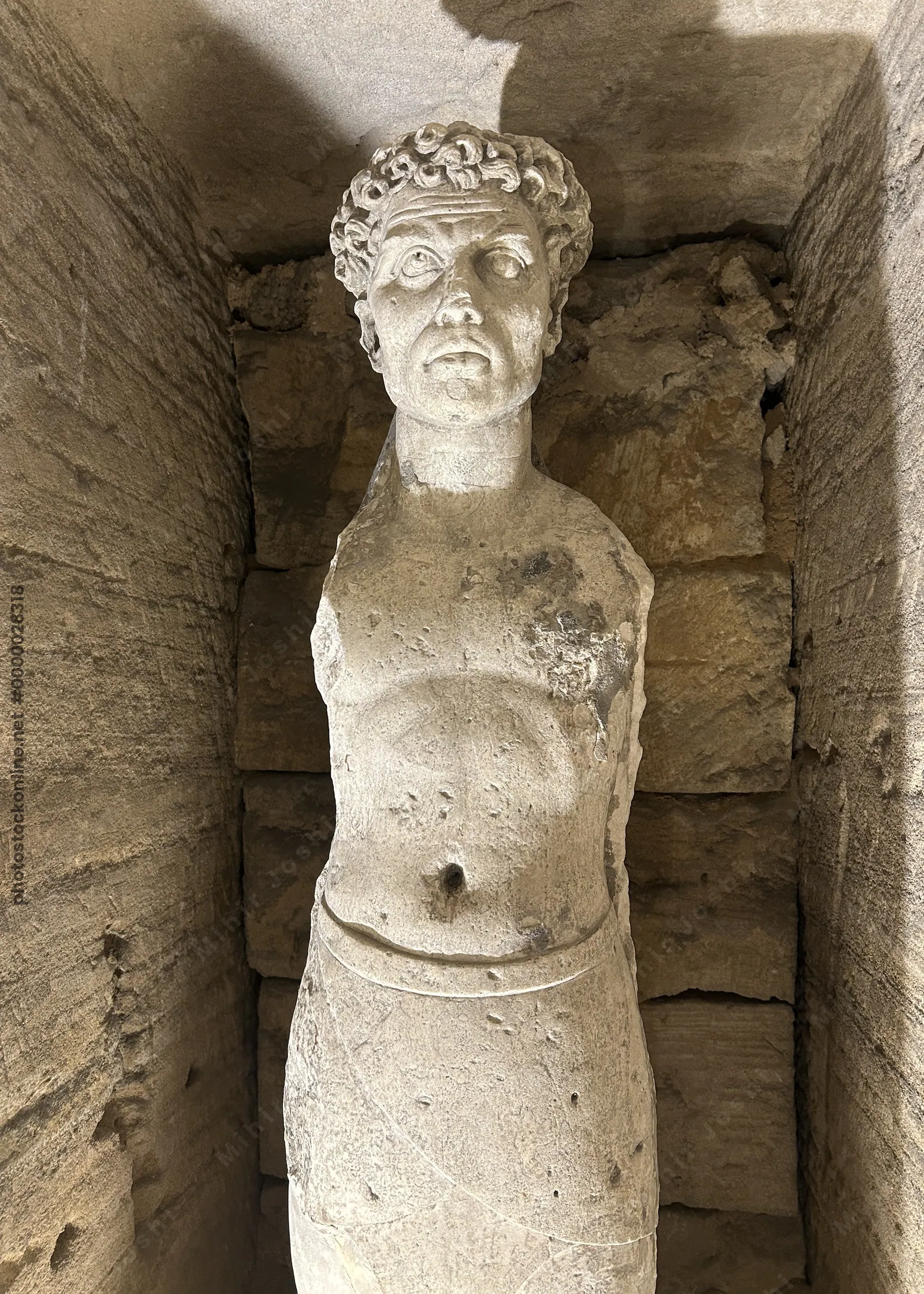 Alexandria, Egypt - Feb 13, 2025: Weathered statue of a male figure with curly hair inside the Catacombs of Kom El Shoqafa, a Greco-Roman necropolis i