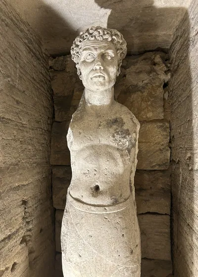 Alexandria, Egypt - Feb 13, 2025: Weathered statue of a male figure with curly hair inside the Catacombs of Kom El Shoqafa, a Greco-Roman necropolis i