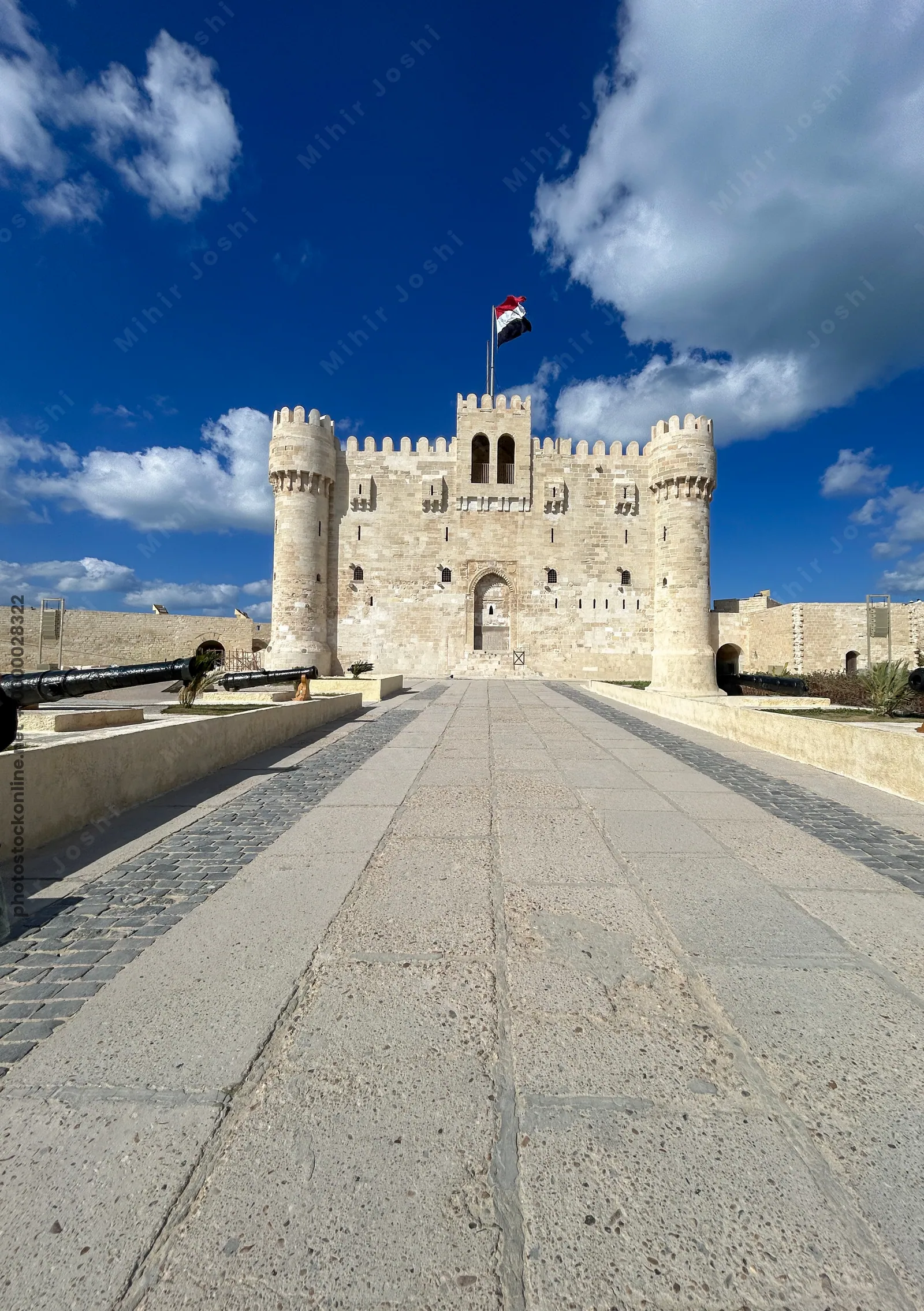 Alexandria, Egypt - Feb 13, 2025: Front view of the medieval Citadel of Qaitbay fortress with Egyptian flag and cannons on display, located on the Med