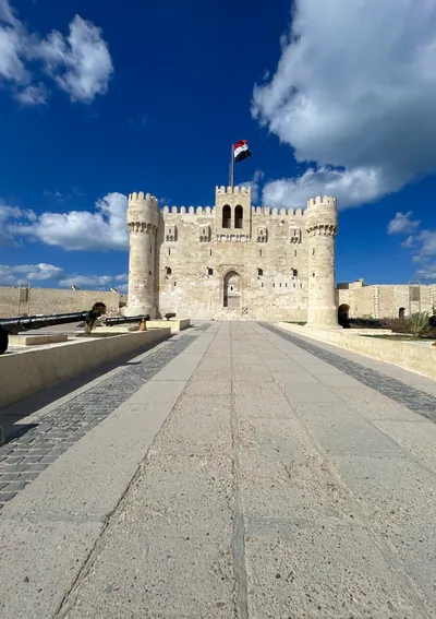 Alexandria, Egypt - Feb 13, 2025: Front view of the medieval Citadel of Qaitbay fortress with Egyptian flag and cannons on display, located on the Med