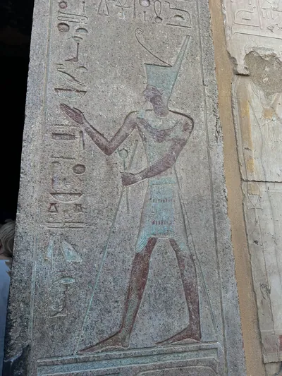 Luxor, Egypt - Feb 11, 2025: Ancient carved relief of a pharaoh wearing the tall crown and holding a staff, from the doorway of the Mortuary Temple of