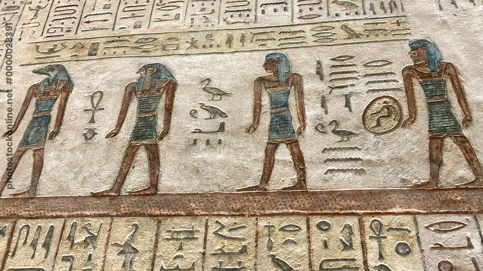 Luxor, Egypt - Feb 11, 2025: Ancient painted wall relief depicting a procession of deities, including a jackal-headed figure, with hieroglyphic inscri