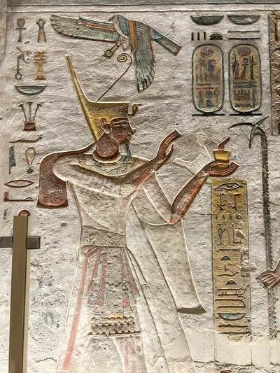 Luxor, Egypt - Feb 11, 2025: Ancient painted wall relief of Ramesses III wearing the tall crown and presenting an offering, with hieroglyphs and carto