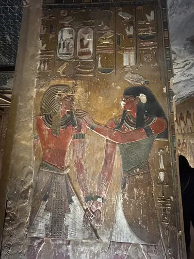 Luxor, Egypt - Feb 11, 2025: Ancient painted wall relief showing the god Geb with a pharaoh, accompanied by hieroglyphs, in a tomb at the Valley of th