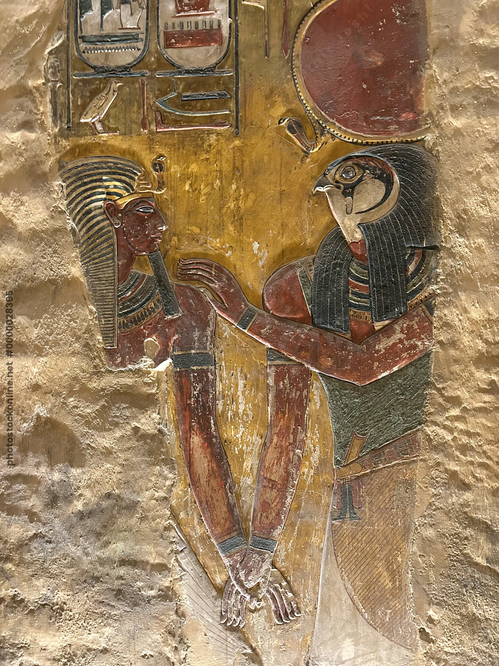 Luxor, Egypt - Feb 11, 2025: Ancient painted wall relief showing a falcon-headed god with solar disk embracing a pharaoh, with hieroglyphs, in a tomb