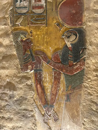 Luxor, Egypt - Feb 11, 2025: Ancient painted wall relief showing a falcon-headed god with solar disk embracing a pharaoh, with hieroglyphs, in a tomb