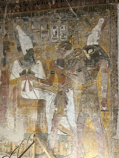 Luxor, Egypt - Feb 11, 2025: Ancient painted wall relief depicting Osiris, Seti I, and Horus inside KV17, the tomb of Seti I, in the Valley of the Kin