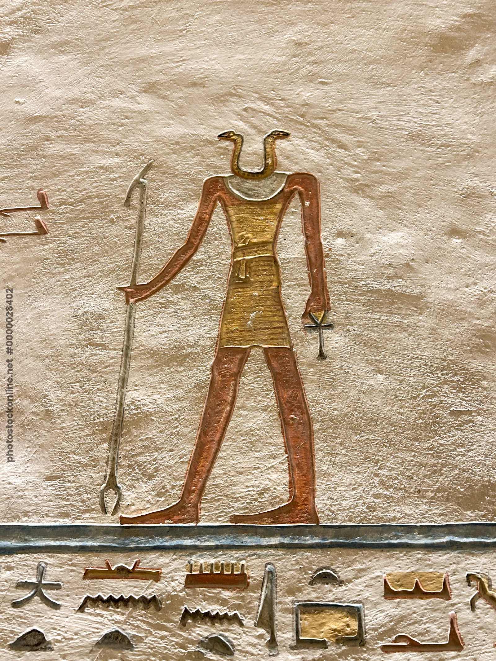 Luxor, Egypt - Feb 11, 2025: Ancient wall relief showing a serpent-headed deity holding a staff and ankh, carved and painted in a tomb at the Valley o