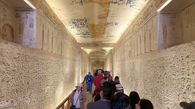 Luxor, Egypt - 11-Feb-2025: Tourists walk through a decorated corridor inside a tomb in the Valley of the Kings, with walls and ceilings covered in an
