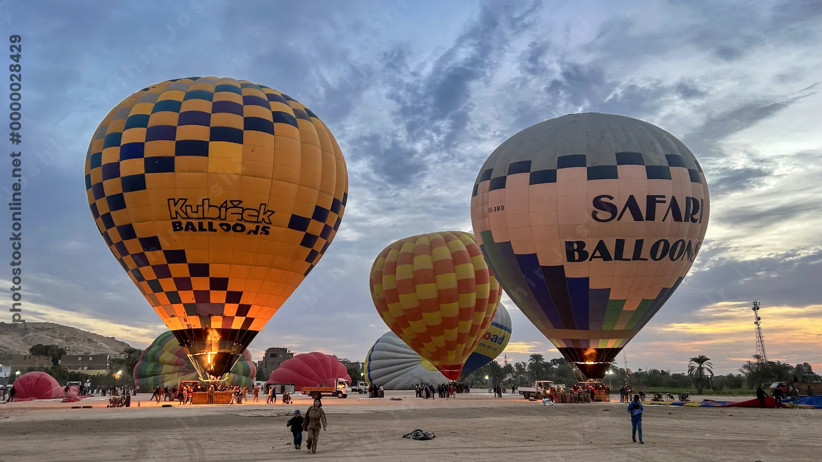 Luxor, Egypt - Feb 10, 2025: Colorful hot air balloons being inflated before sunrise, with flames lighting the scene and tourists preparing for flight