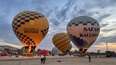 Luxor, Egypt - Feb 10, 2025: Colorful hot air balloons being inflated before sunrise, with flames lighting the scene and tourists preparing for flight