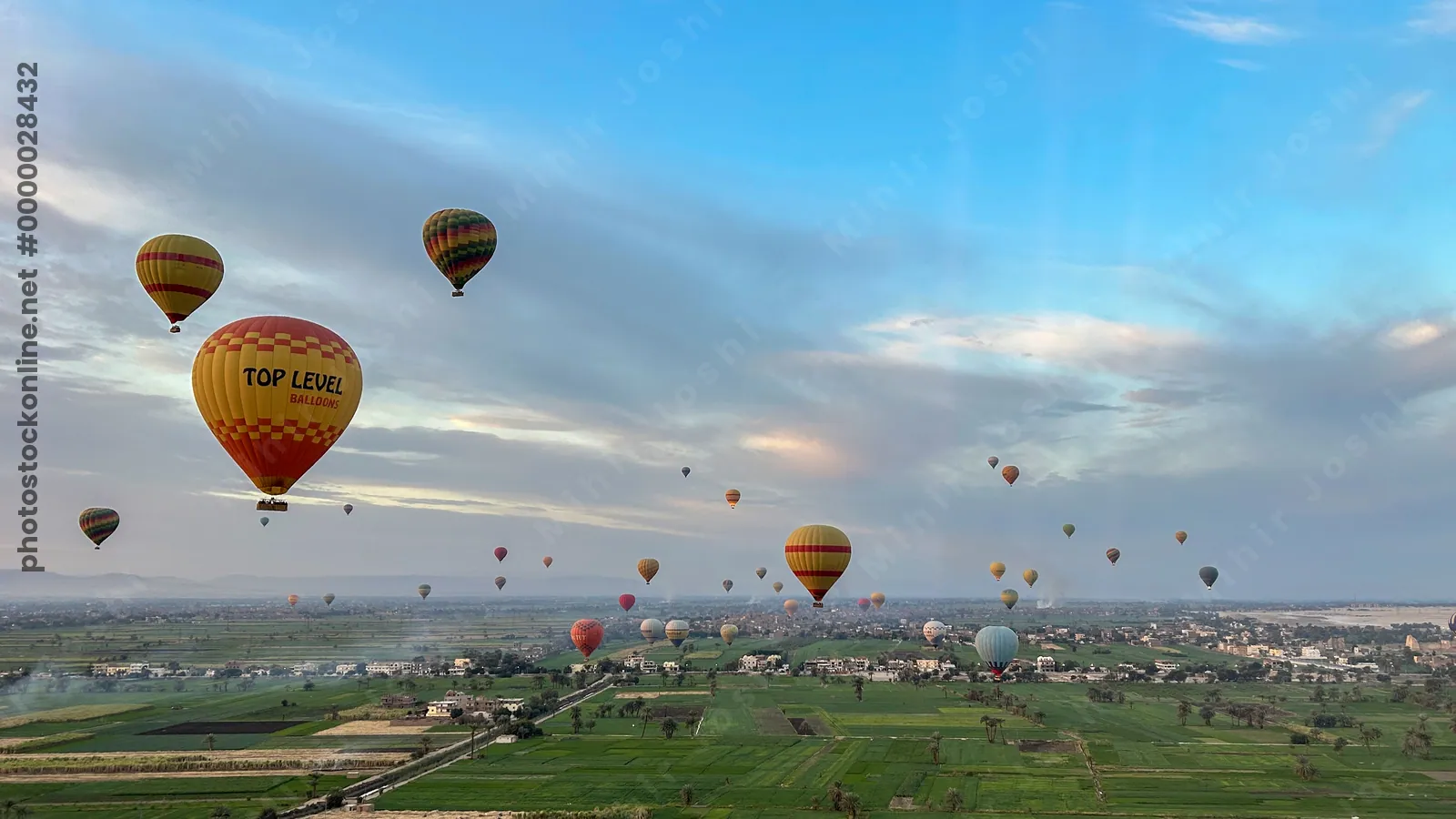 Luxor, Egypt - Feb 10, 2025: Colorful hot air balloons drifting above lush green fields at sunrise, offering a scenic aerial view of the landscape.