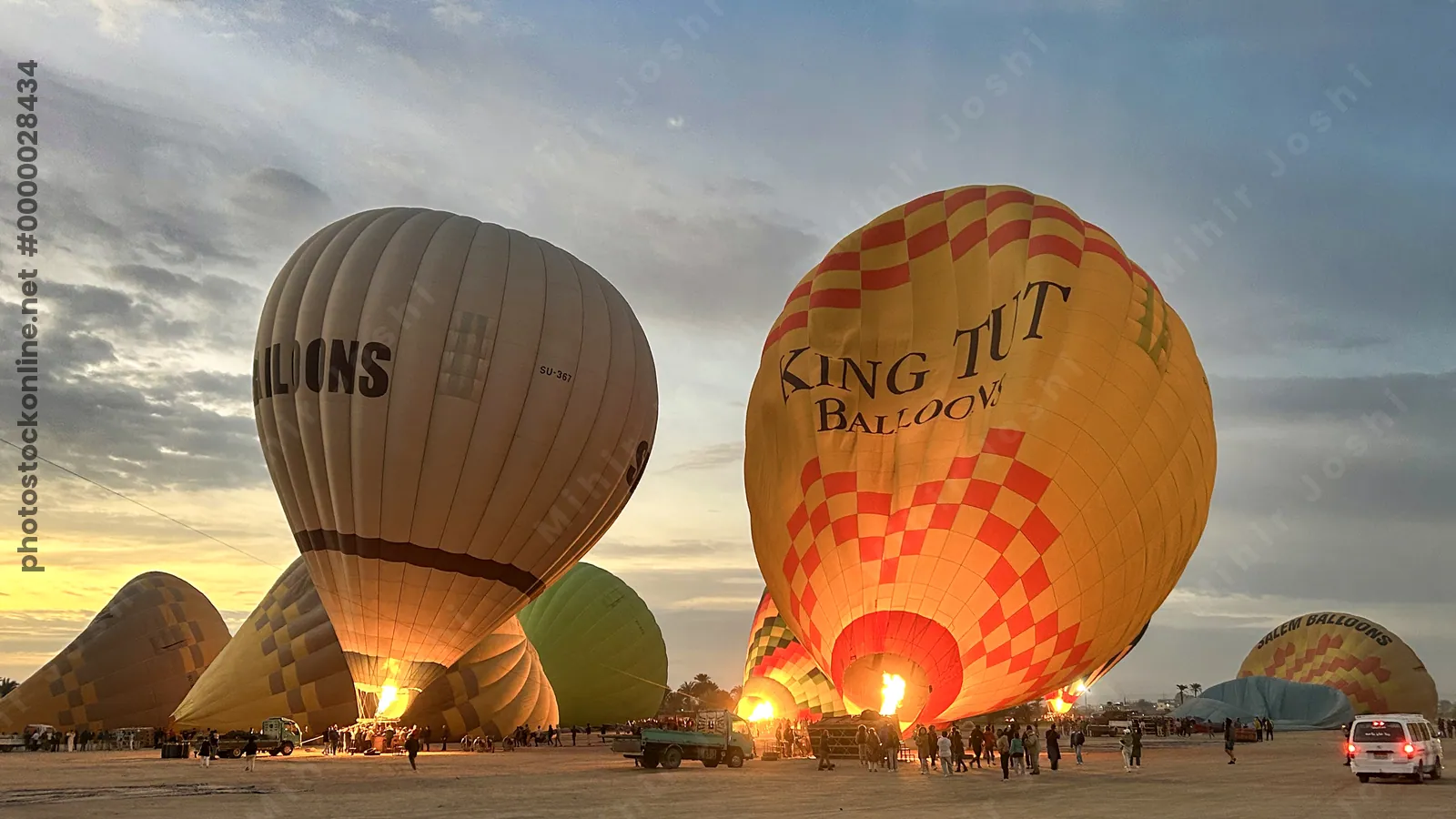 Luxor, Egypt - Feb 10, 2025: Colorful hot air balloons being inflated before sunrise, with flames lighting the scene and tourists preparing for flight