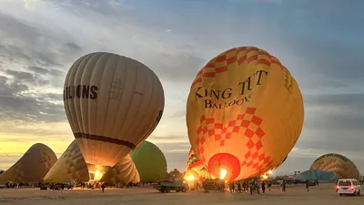Luxor, Egypt - Feb 10, 2025: Colorful hot air balloons being inflated before sunrise, with flames lighting the scene and tourists preparing for flight
