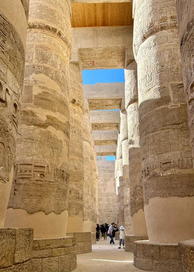 Karnak Temple, Luxor, Egypt - Feb 10, 2025: Massive sandstone columns with detailed hieroglyphics inside the Great Hypostyle Hall, with visitors explo