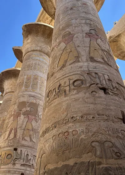 Luxor, Egypt - Feb 10, 2025: Massive sandstone columns with painted reliefs and hieroglyphs inside the Hypostyle Hall of Karnak Temple in Luxor, Egypt