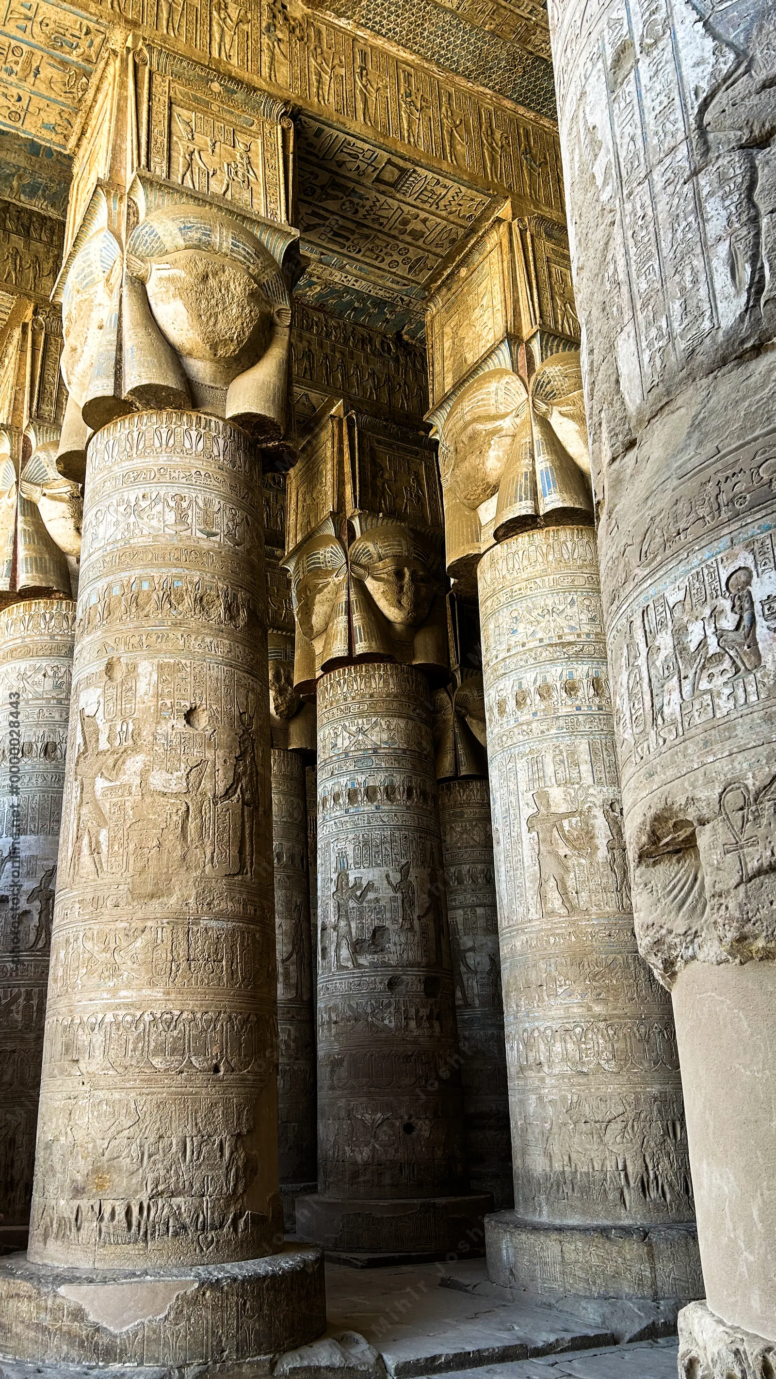 Ancient hieroglyphs and carved columns with painted ceiling details inside Dendera Temple in Egypt.
