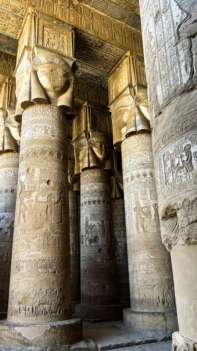 Ancient hieroglyphs and carved columns with painted ceiling details inside Dendera Temple in Egypt.