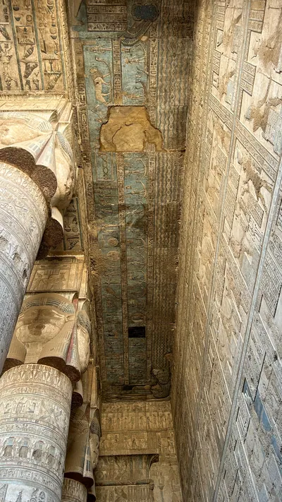 Ancient hieroglyphs and carved columns with painted ceiling details inside Dendera Temple in Egypt.