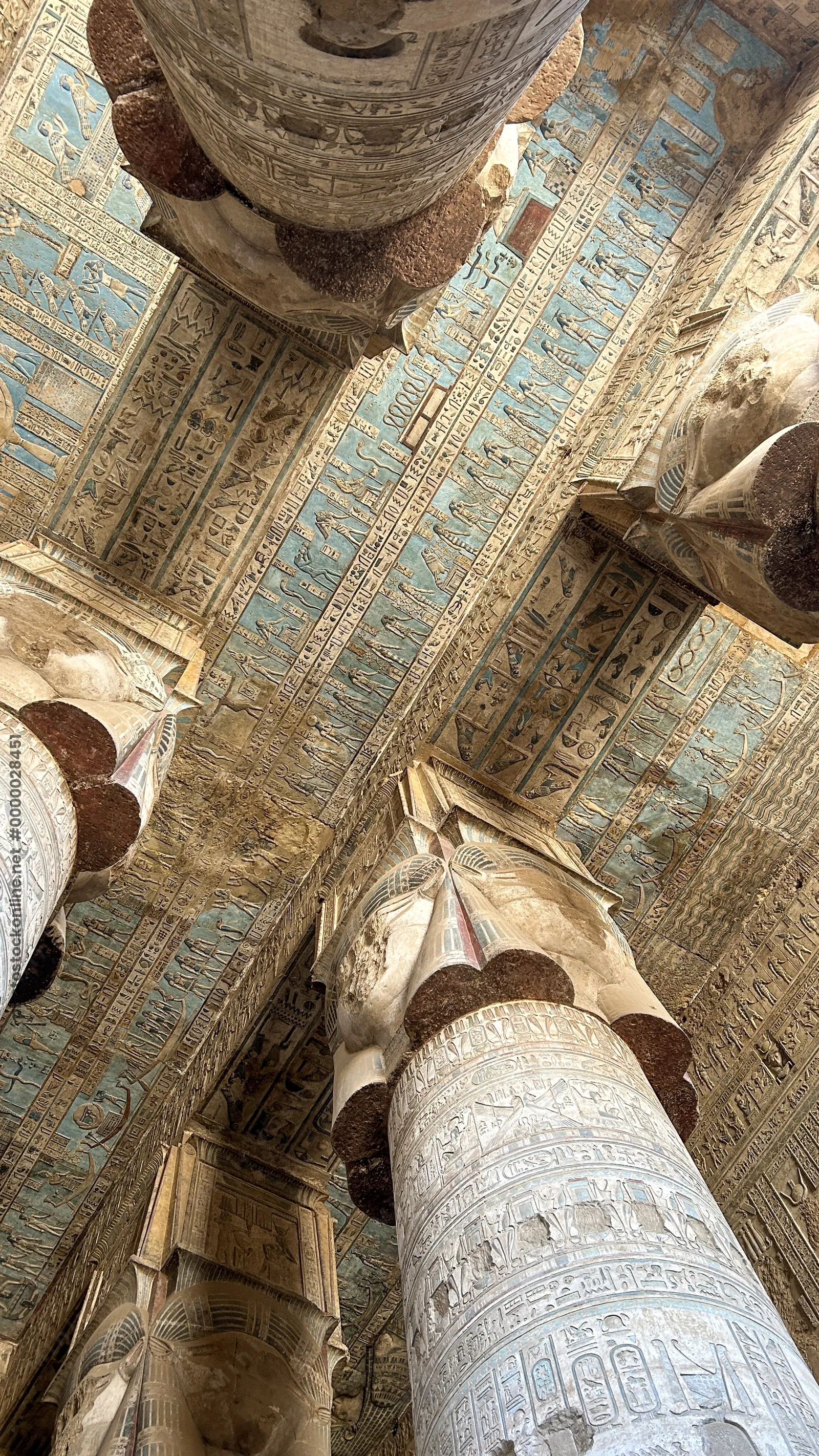 Ancient hieroglyphs and carved columns with painted ceiling details inside Dendera Temple in Egypt.